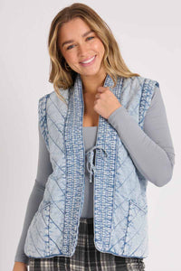 ellis & dewey quilted vest puff like fabric in a light denim look fabric. ties at the front. close up of photo