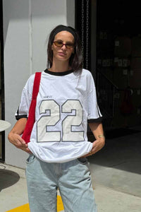 ssaint oversized white t shirt with black binding around neck and sleeve, two black stripes down sleeve but twenty two number on front in whitee with black edging worn on model with jeans